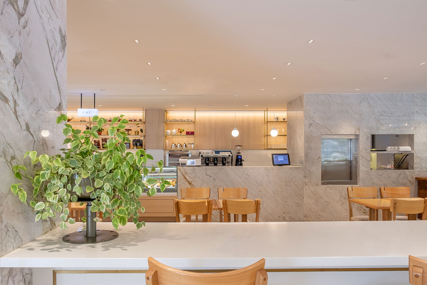 Interior da confeitaria Casa Doce, com um balcão de mármore branco e cadeiras de madeira.